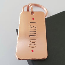 Load image into Gallery viewer, Copper keyring, hand stamped I STILL DO, with red hearts. 40mm x 20mm, textured around the edges. Large and small split rings.