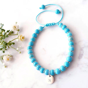 Blue beaded bracelet with rings in between each bead a personalised circle charm. Adjustable cord bracelet.